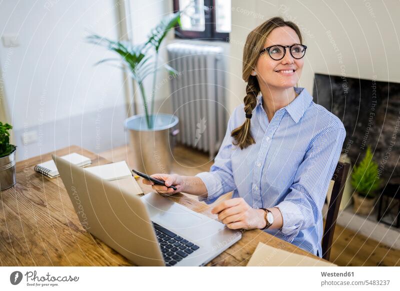Smiling woman sitting at wooden desk at home looking sideways looking away look away desks females women Seated smiling smile view seeing viewing Table Tables