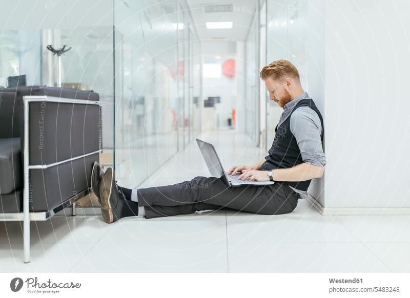 Businessman in office sitting on floor, using laptop Laptop Computers laptops notebook working At Work Seated offices office room office rooms floors computer