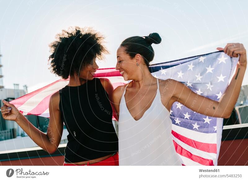 Female friends holding US American flag, standing on rooftop lesbian smiling smile carefree Fun having fun funny female friends American Flag American Flags