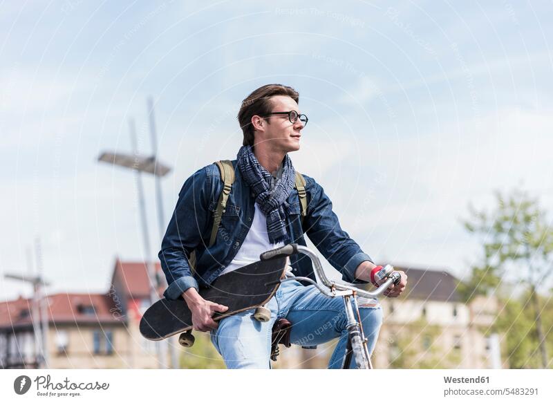 Young man holding skateboard riding bicycle in the city riding bike bike riding cycling bicycling pedaling Skate Board skateboards bikes bicycles men males