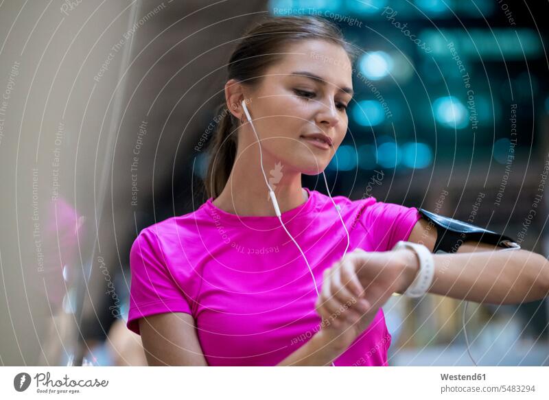 Young woman in pink sportshirt listening to music and checking her smartwatch earphones ear phone ear phones young women young woman smart watch Listening Music