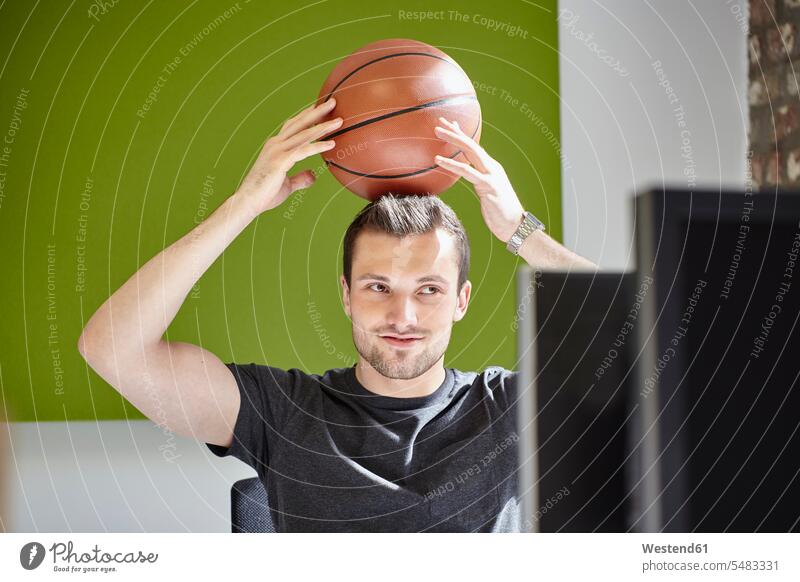 Young man working in office, balancing a basketball portrait portraits At Work sitting Seated balls balance offices office room office rooms Basketball thinking