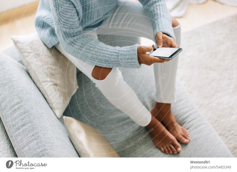 Young woman sitting on couch using smartphone, partial view females women Seated Adults grown-ups grownups adult people persons human being humans human beings
