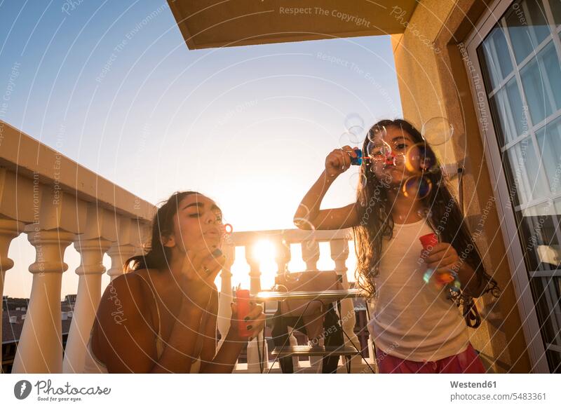 Teenage girl and her little sister blowing soap bubbles on balcony relaxed relaxation happiness happy sisters females girls Fun having fun funny relaxing