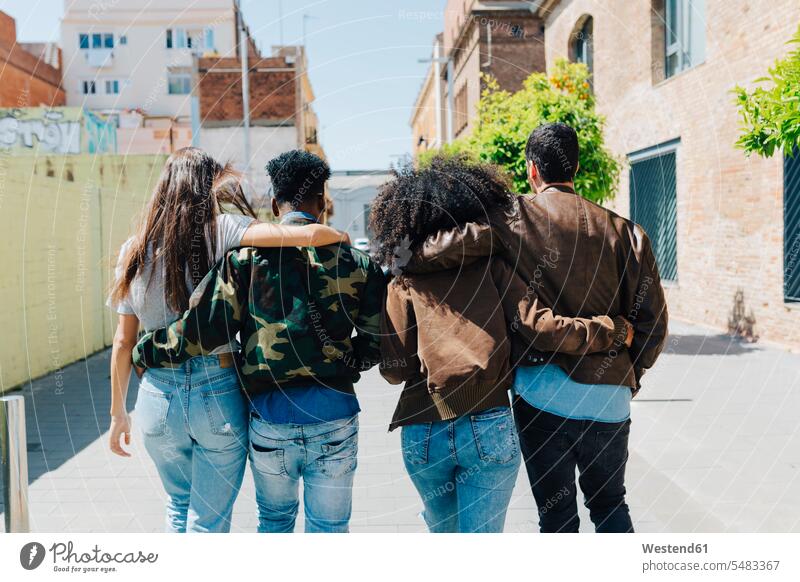 Rear view of stylish friends walking on urban street going embracing embrace Embracement hug hugging on the move on the way on the go on the road friendship