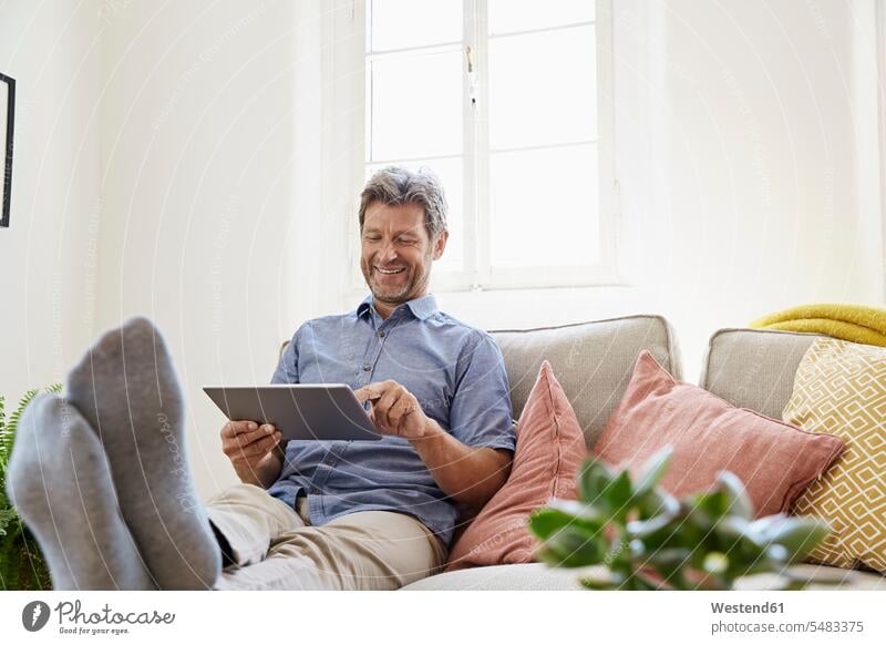 Man sitting on couch at home, using digital tablet online Seated relaxation relaxed relaxing man men males comfortable Surfing the Net Internet The Internet