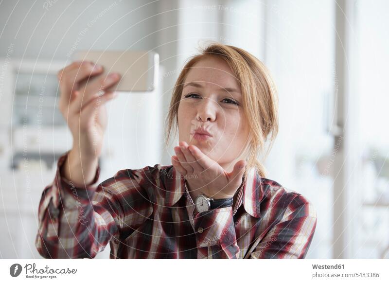 Young woman blowing a kiss while taking a selfie with her smartphone shirt shirts strand of hair self-portrait Self Portrait Photography Photographing Self