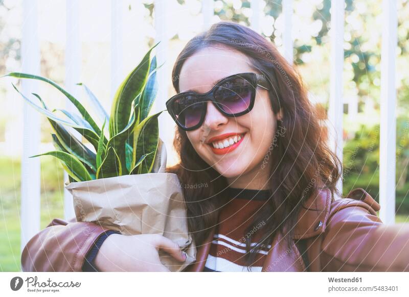 Portrait of smiling young woman with potted plant taking selfie with smartphone portrait portraits females women Selfie Selfies Adults grown-ups grownups adult