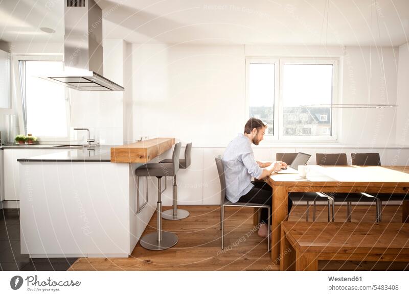 Man sitting at table in his open plan kitchen using laptop accessibility accessible Seated lifestyle life styles Dining Table Dinner Table Dining Tables
