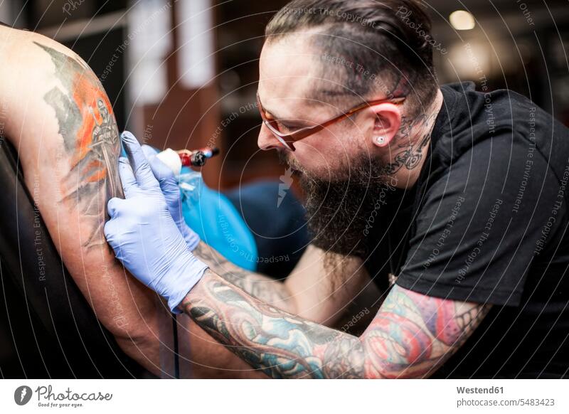 Tattoo artist tattooing an arm tattooist tattooer tattoos tattooed body art Body Adornment Skin Art style stylish studio studios man males Adults grown-ups