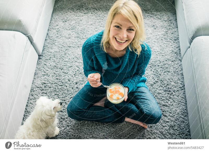 Portrait of happy woman with dog eating fruit yoghurt in living room smiling smile dogs Canine sitting Seated Yogurt Yoghurt Yoghourt females women living rooms