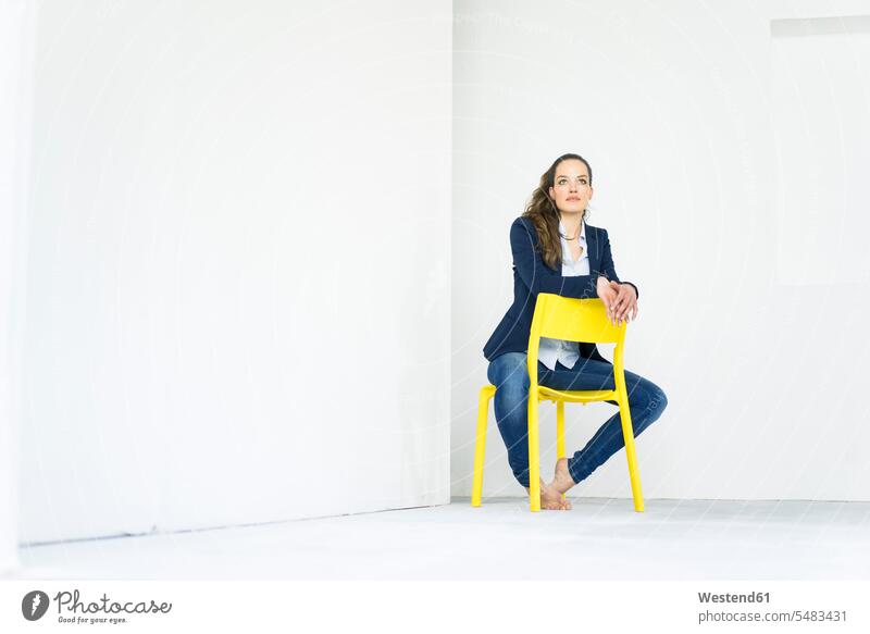 Businesswoman sitting on a yellow chair thinking chairs businesswoman businesswomen business woman business women Seated females business people businesspeople