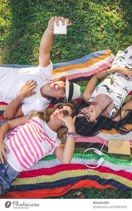 Playful friends lying on blanket in park taking a selfie laying down lie lying down mobile phone mobiles mobile phones Cellphone cell phone cell phones Selfie