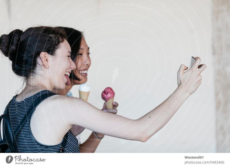 Two young women with ice cream cones taking selfie with smartphone female friends Selfie Selfies mate friendship eating laughing Laughter Smartphone iPhone