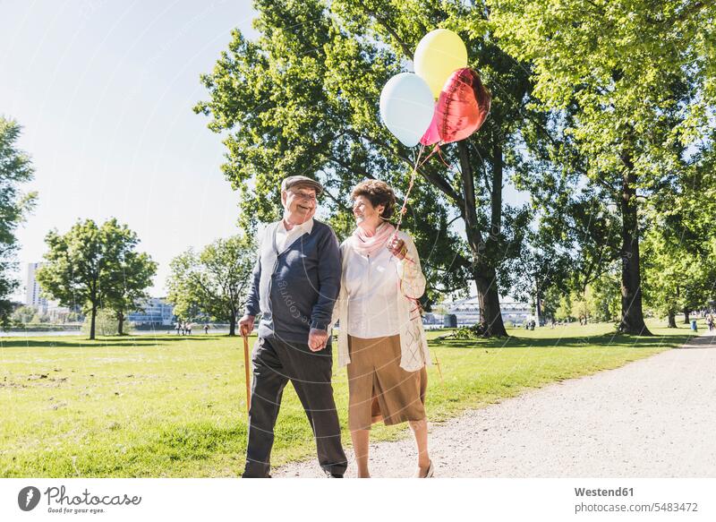 Happy senior couple with balloons strolling in a park elder couples senior couples adult couple adult couples twosomes partnership people persons human being