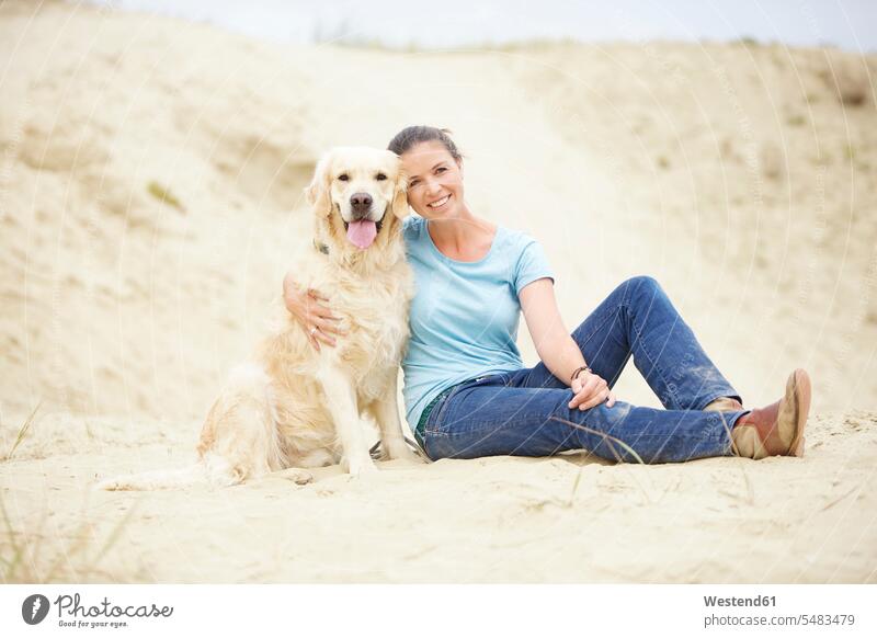 Smiling young woman with dog in sand smiling smile sandy females women dogs Canine Adults grown-ups grownups adult people persons human being humans