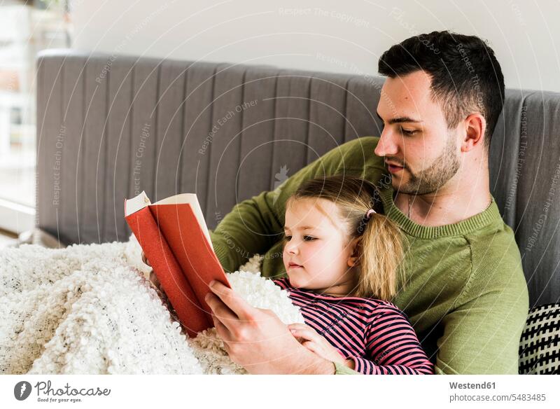 Father and daughter reading a book at home daughters father pa fathers daddy dads papa lying laying down lie lying down child children family families people