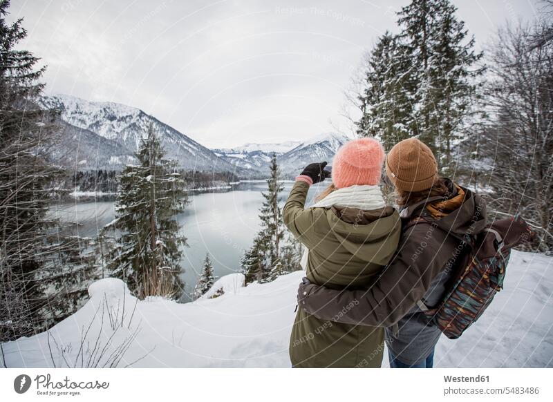 Couple taking a picture in alpine winter landscape with lake hibernal lakes photographing landscapes scenery terrain couple twosomes partnership couples Alps