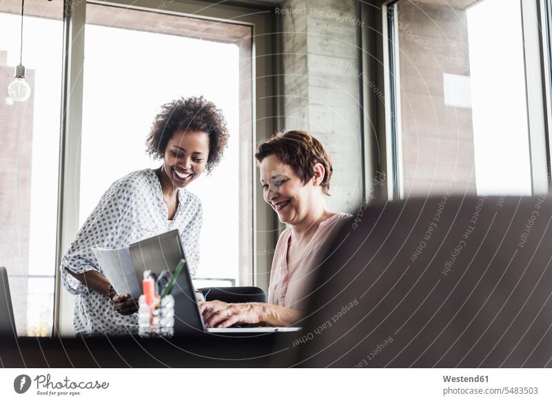 Two smiling women working together in an office offices office room office rooms At Work Female Colleague workplace work place place of work colleagues