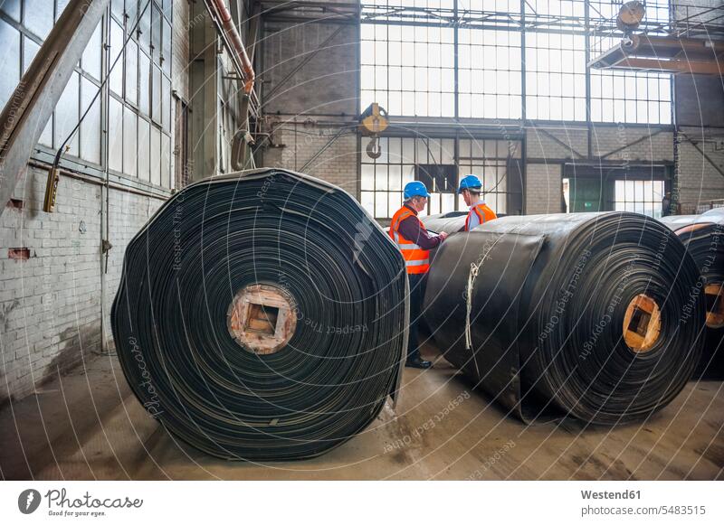Two men with safety vests in factory hall with rolls of rubber caucasian caucasian ethnicity caucasian appearance european factory workshop factory floor