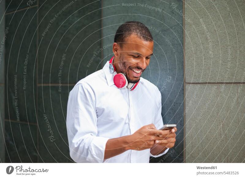 Smiling businessman with headphones looking at smartphone Businessman Business man Businessmen Business men smiling smile business people businesspeople