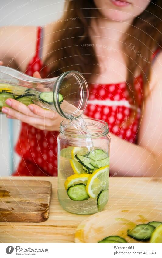 Woman pouring detox water infused with lemon and cucumber into a glass woman females women soft drink refreshing drink soft drinks refreshing drinks Adults