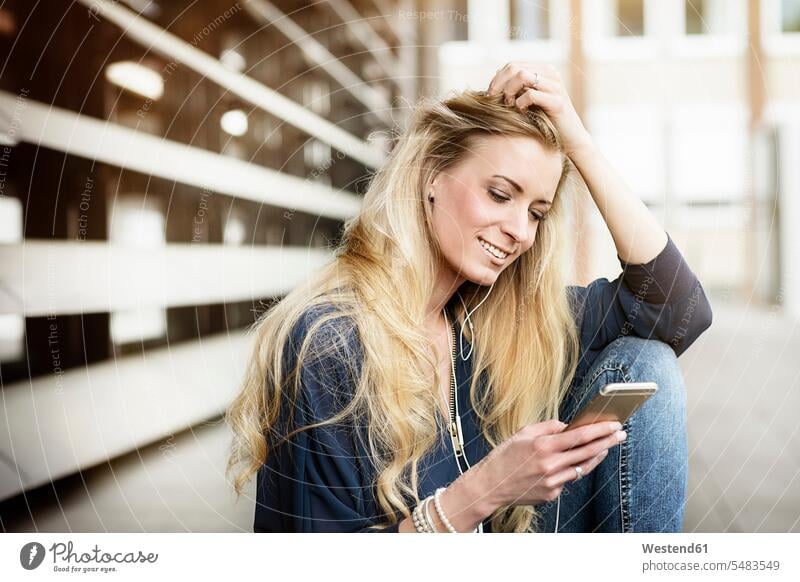 Portrait of smiling blond young woman with earphones looking at cell phone females women portrait portraits Adults grown-ups grownups adult people persons