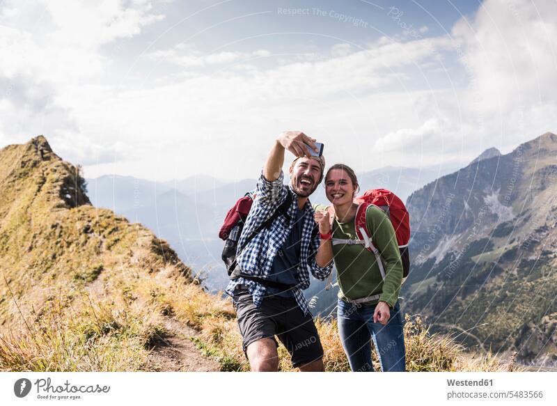 Germany, Bavaria, Oberstdorf, happy couple taking a selfie on mountain ridge twosomes partnership couples mountain range mountains mountain ranges mobile phone