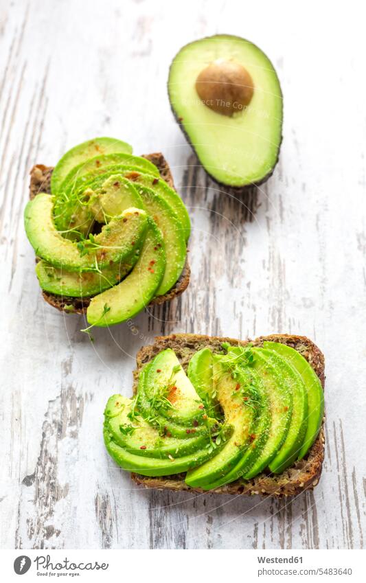 Protein bread garnished with sliced avocado, cress and chili powder green wooden half halves halved hearty savoury food lusty cresses ready to eat ready-to-eat