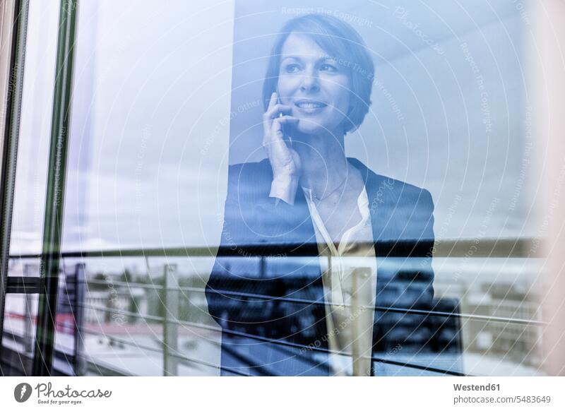 Businesswoman on cell phone behind windowpane caucasian caucasian ethnicity caucasian appearance european telecommunication telecommunications Germany