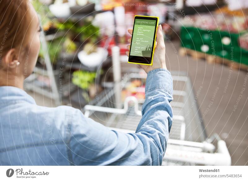 Woman holding a smart phone with a shopping list in front of a super market lists supermarket mobile phone mobiles mobile phones Cellphone cell phone