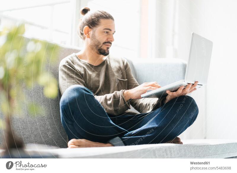 Portrait of man sitting on the couch using laptop men males Laptop Computers laptops notebook Adults grown-ups grownups adult people persons human being humans