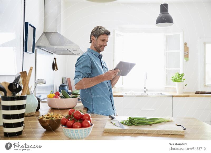 Mature man in his kitchen reading recipe on his digital tablet men males confidence confident cooking digitizer Tablet Computer Tablet PC Tablet Computers iPad