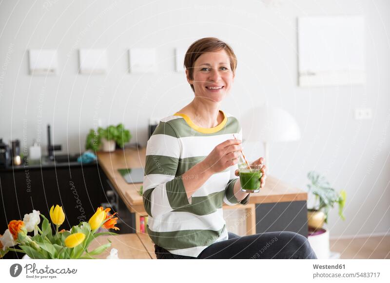 Portrait of smiling woman with green smoothie in the kitchen females women Smoothies portrait portraits Adults grown-ups grownups adult people persons