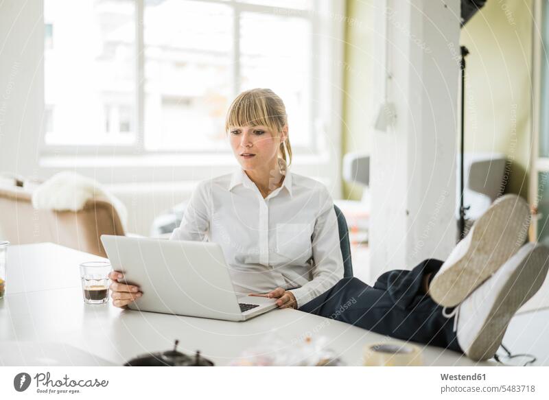 Businesswoman using laptop in office with feet on desk Laptop Computers laptops notebook offices office room office rooms desks businesswoman businesswomen