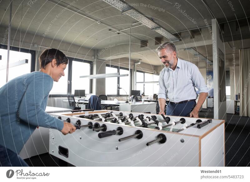 Two colleagues playing foosball in office businesswoman businesswomen business woman business women smiling smile Businessman Business man Businessmen