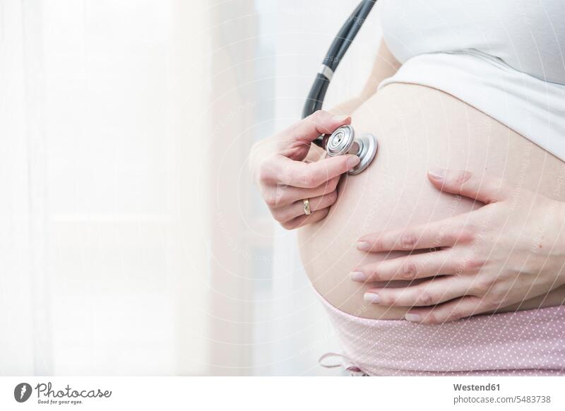 Pregnant woman holding stethoscope in front of her belly caucasian caucasian ethnicity caucasian appearance european bellies abdomen human abdomen midsection