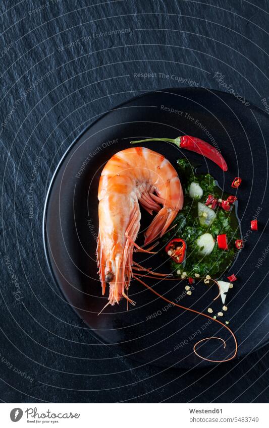 Prawn with hernbs, chili and garlic on black plate Plate dish dishes Plates dark background herbs olive oil seafood black background black backgrounds