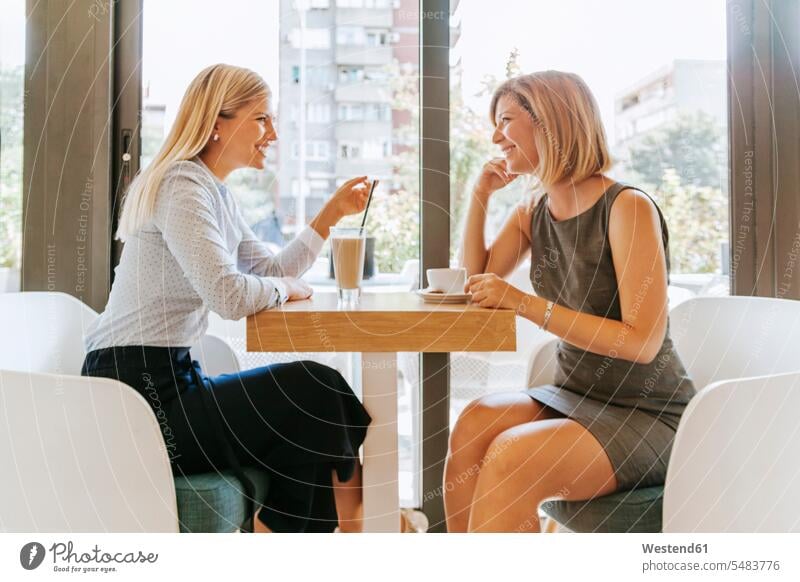 Two young women meeting in a cafe talking speaking female friends smiling smile mate friendship opposite togetherness face to face Facing Each Other