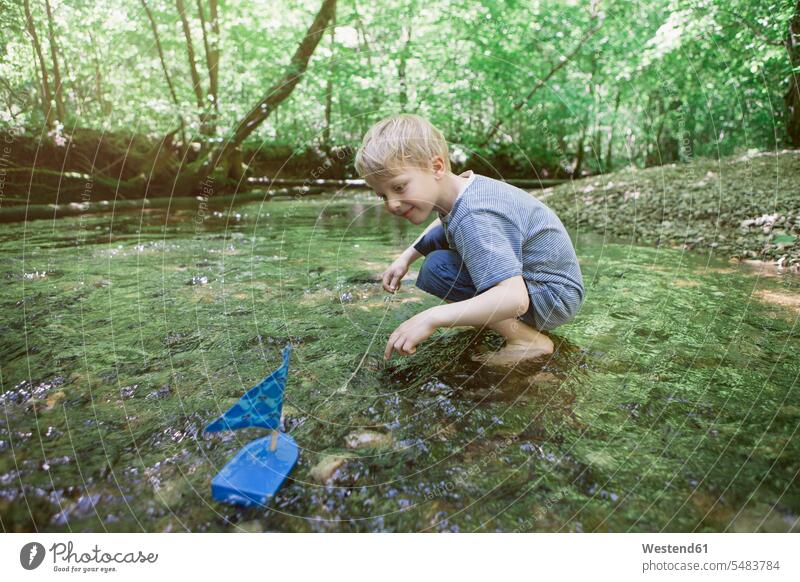 Boy playing with a toy boat in a forest brook water boats Toy Boat boy boys males child children kid kids people persons human being humans human beings