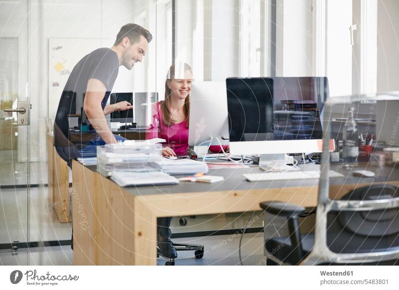 Man and woman working in office, smiling Female Colleague sitting Seated At Work together Office Offices colleagues Germany teamwork teamworking computer