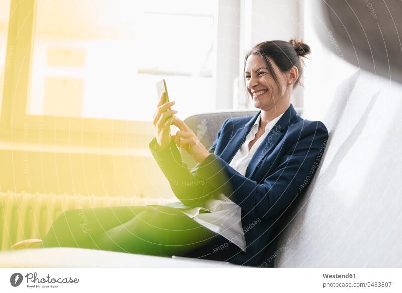 Laughing businesswoman sitting on a couch using her cell phone businesswomen business woman business women Selfie Selfies females Smartphone iPhone Smartphones