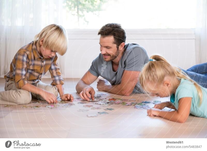 Father with two children lying on the floor at home playing jigsaw puzzle floors laying down lie lying down father pa fathers daddy dads papa family families