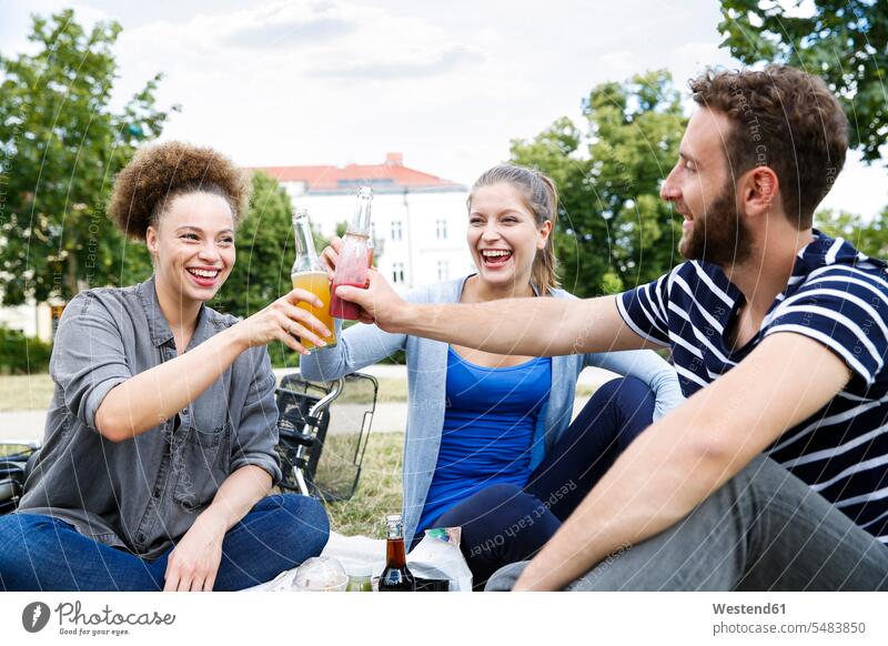 Three happy friends clinking bottles in park toasting cheers Bottle Bottles laughing Laughter happiness friendship positive Emotion Feeling Feelings Sentiments