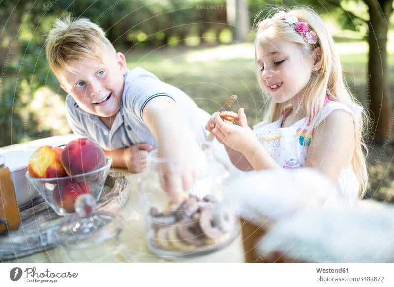 Sister and brother eating cakes at garden table brothers smiling smile Biscuit Cookie Cooky Cookies Biscuits sister sisters siblings brother and sister
