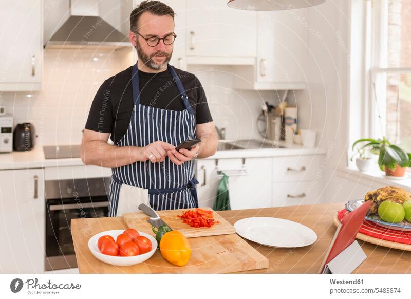 Portrait of man using smartphone while preparing food in the kitchen texting sending bell pepper Paprika pepper vegetable capsicum Paprikas bell peppers