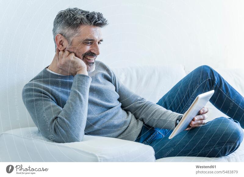 Smiling mature man at home using tablet couch settee sofa sofas couches settees men males digitizer Tablet Computer Tablet PC Tablet Computers iPad