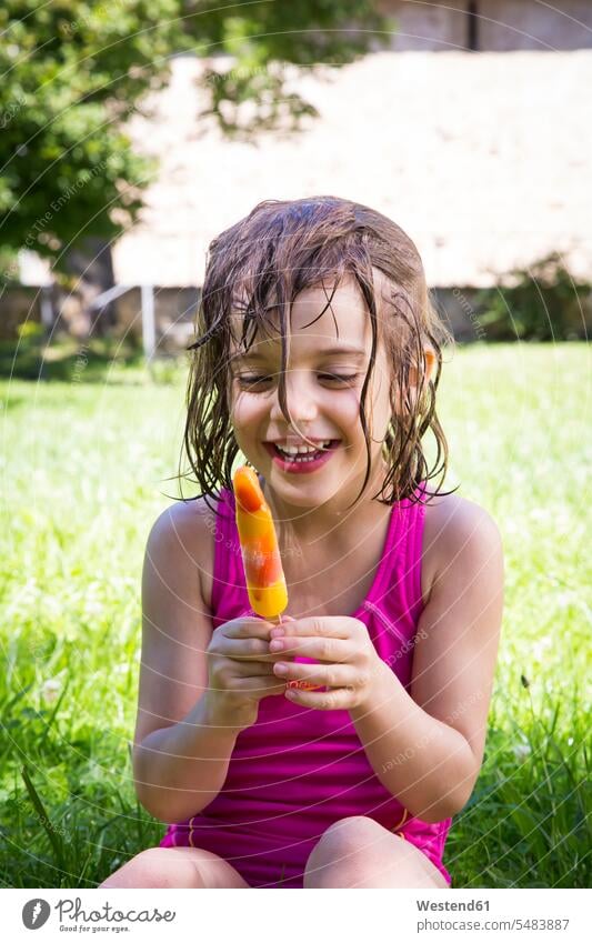 Portrait of happy little girl with wet hair sitting on a meadow with ice lolly females girls dining eat eating child children kid kids people persons