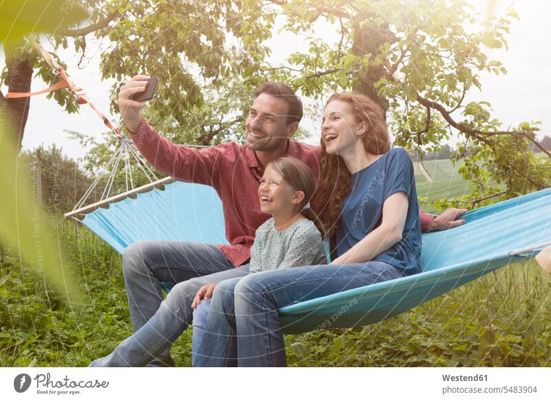 Happy family sitting in hammmock taking a selfie garden gardens domestic garden daughter daughters mobile phone mobiles mobile phones Cellphone cell phone