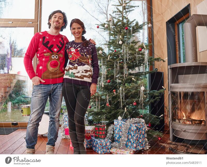 Couple standing in front of Christmas tree wearing Christmas jumpers caucasian caucasian ethnicity caucasian appearance european bonding community Christmas Eve